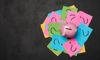 Ceramic piggy bank and stickers with drawn question marks on a black background, top view photo