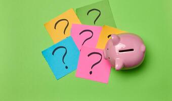 Ceramic piggy bank and stickers with drawn question marks on a green background, top view photo