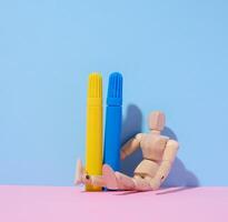 Wooden mannequin holding two felt-tip pens on blue background photo