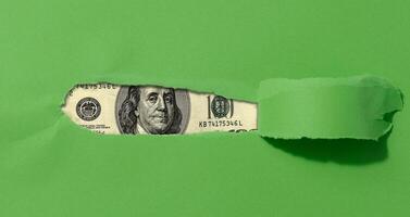 A green sheet of paper with a torn middle and a curled edge, a hundred dollar bill in the hole. photo