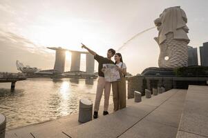 merlion fuente en frente de el centro de deportes acuáticos bahía playa con joven asiático Pareja de amor turista. foto