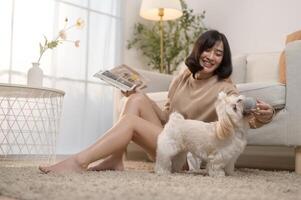 Happy young asian woman cuddling and spending time with cute dog in living room. photo