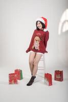 Young happy woman in santa claus hat wearing red sweater over white background, Christmas concept photo