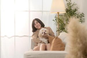 contento joven asiático mujer acurrucarse y gasto hora con linda perro en vivo habitación. foto