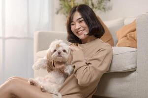 Happy young asian woman cuddling and spending time with cute dog in living room. photo
