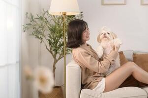 Happy young asian woman cuddling and spending time with cute dog in living room. photo