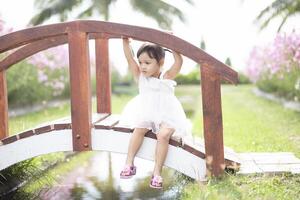 A young girl sits on a wooden bridge happily watching the flowers bloom. photo