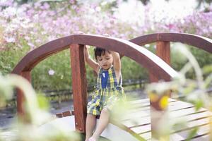 un joven niña se sienta en un de madera puente felizmente acecho el flores floración. foto