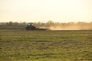 tractor a puesta de sol arado arado un campo. labranza el suelo en el otoño después cosecha. el final de el temporada foto