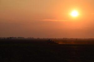 Tractor plowing plow the field on a background sunset. tractor silhouette on sunset background photo