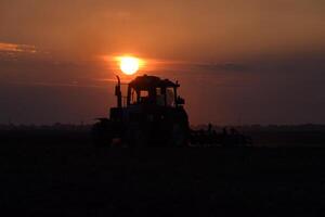 tractor arada arado el campo en un antecedentes puesta de sol. tractor silueta en puesta de sol antecedentes foto