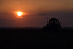 Tractor plowing plow the field on a background sunset. tractor silhouette on sunset background photo