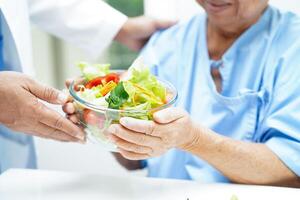 Asian elderly woman patient eating salmon stake and vegetable salad for healthy food in hospital. photo