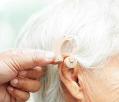 Doctor install hearing aid on senior patient ear to reduce hearing loss problem. photo