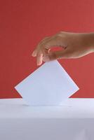 Female Hand Voting Near Ballot Box on Red Background photo