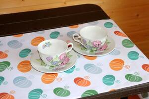 Two porcelain white empty tea cups with flowers on a table runner printed with colorful pumpkins. Waiting for guests, preparing for tea, autumn table setting, home comfort, horizontal photo. photo