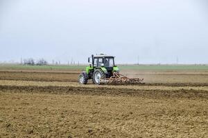 lozano y aflojar el suelo en el campo antes de siembra. el tractor arados un campo con un arado foto