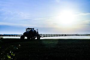 tractor con el ayuda de un rociador aerosoles líquido fertilizantes en joven trigo en el campo. foto