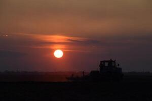 tractor arada arado el campo en un antecedentes puesta de sol. tractor silueta en puesta de sol antecedentes foto