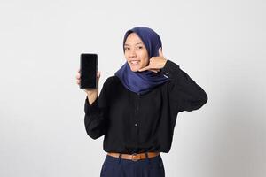 Portrait of excited Asian hijab woman in casual shirt showing blank screen mobile phone mockup while pointing and presenting product. Isolated image on white background photo