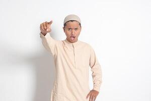 Portrait of attractive Asian muslim man in koko shirt making angry hand gesture with fingers, scolding someone who has done something wrong. Isolated image on white background photo