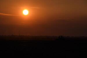 tractor arada arado el campo en un antecedentes puesta de sol. tractor silueta en puesta de sol antecedentes foto