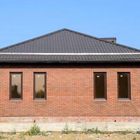 The house with plastic windows and a roof of corrugated sheet. Brown roof and brown brick photo