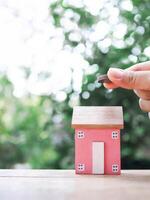 Close up hand putting coin with miniature house. The concept of saving money for house, Property investment, House mortgage, Real estate. photo