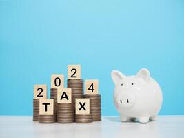 Wooden block with word TAX and number 2024 on stack of coins. The concept of saving money for business achievement goal, Financial, Investment and Business growing in year 2024. photo