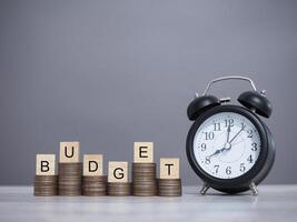 Alarm clock and Wooden blocks with the word BUDGET on stack of coins. The concept about budget planning and allocation photo