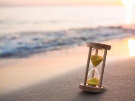 Hourglass on the beach in the sunset time. The concept about countdown to Summer, Travel, Vacation and Relaxation. photo