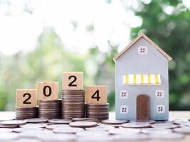 Miniature house, Wooden blocks with number 2024 on stack of coins. The concept of payment tax for house, Property investment, House mortgage, Real estate in New Year 2024. photo