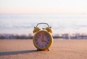 Yellow alarm clock on the beach in the sunset time. The concept about Time to summer, Travel, Vacation and Relaxation photo
