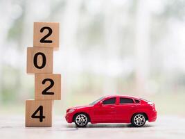 de madera bloquear con número 2024 y juguete coche. el concepto de ahorro dinero para coche préstamo, seguro, pago impuesto en año 2024 foto