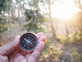 cerca arriba de Brújula en mujer mano con bosque en el puesta de sol hora como antecedentes. el concepto de mundo turismo día, buscando el Derecha direcciones y viaje foto