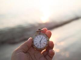 Close up of vintage pocket watch in woman hand with sea in the sunset time as background. photo