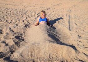 Girl in a bikini on the beach buried in half in the sand. photo