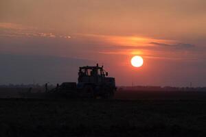 tractor arada arado el campo en un antecedentes puesta de sol. tractor silueta en puesta de sol antecedentes foto