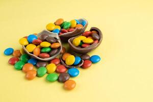 Scattered multi-colored candies in broken Chocolate Easter eggs on yellow background photo