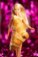 Kyiv, Ukraine, December 16, 2023, Plastic Barbie blond doll dressed in croissant instead of dress on pink foil fringe curtains background photo