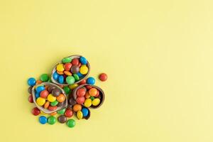 Top view of scattered multi-colored candies in broken Chocolate Easter eggs on yellow background photo