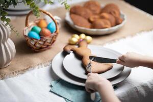 Unrecognizable child cutting gingerbread cookie shaped as Easter bunny at decorated table photo