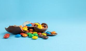 Rainbow candies in broken Chocolate Easter eggs on blue background photo