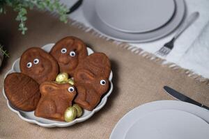 Close-up of Easter muffins shaped as bunnies and eggs with eyes, chocolate eggs on served table setting photo