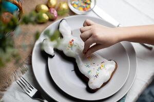 mano de niño decorando horneado Pascua de Resurrección conejito pan de jengibre Galleta con multi de colores azúcar asperja foto