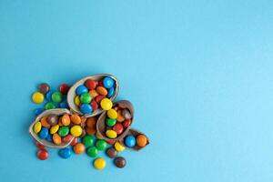 Top view of scattered multi-colored candies in broken Chocolate Easter eggs on blue background photo