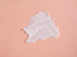 White smear of cosmetic cream on a beige background. Creamy foundation texture isolated. Smear of face cream. Close up of cream texture photo