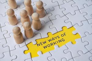 Empty jigsaw puzzle with text - new ways of working surrounded by wooden figures. Business culture photo