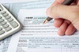 Filling up tax form with tax form and calculator background. Taxation and self assessment concept photo