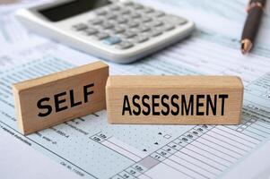 Self assessment text on wooden blocks with tax form and calculator background. Taxation concept photo